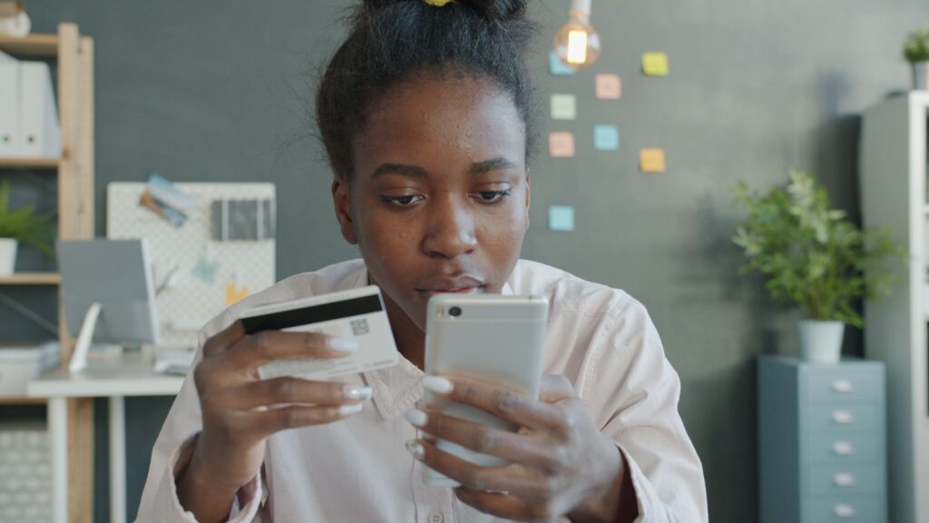 Vrouw met een smartphone en een betaalkaart achter haar laptop