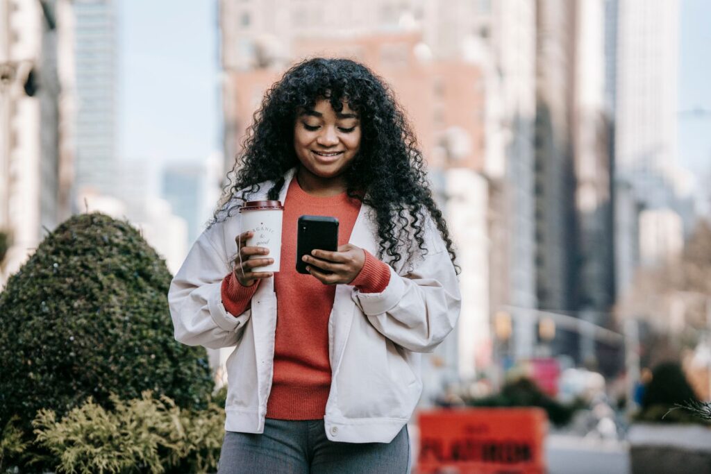 Vrouw met een koffiebeker kijkt op straat op haar telefoon